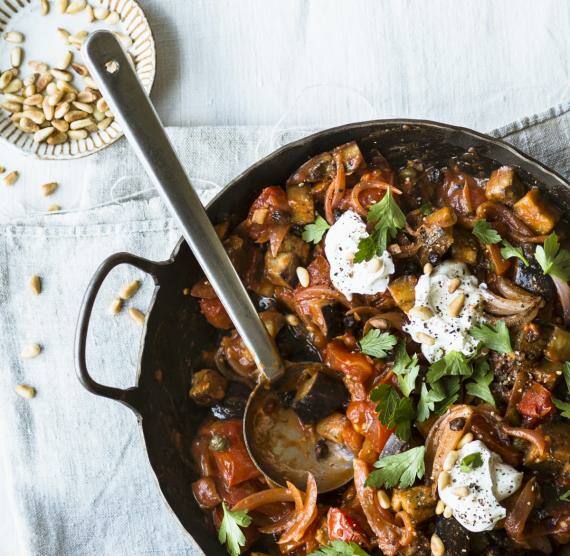 Ragout in einem rustikalen Topf, daneben Pinienkerne in kleiner Schale