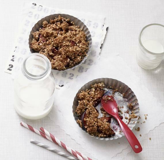 2 Tarteförmchen mit Zwetschgen-Crumble, daneben Milchgläser und Kartenspiel