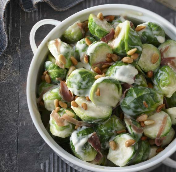 Topf mit Rosenkohl, Sahnesauce, Schinkenstreifen und Pinienkernen