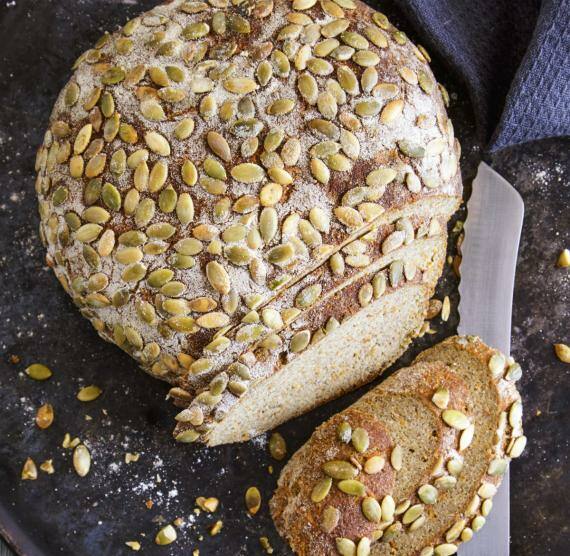 Angeschnittener Brotlaib auf dunklem Teller, darüber Kürbiskerne