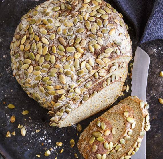 Angeschnittener Brotlaib auf dunklem Teller, darüber Kürbiskerne