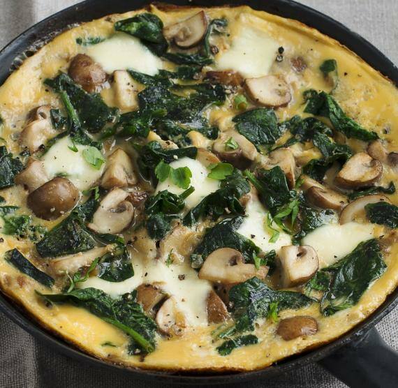 Pfanne mit Omelette mit Pilzen und Spinat, darüber gehackte Petersilie