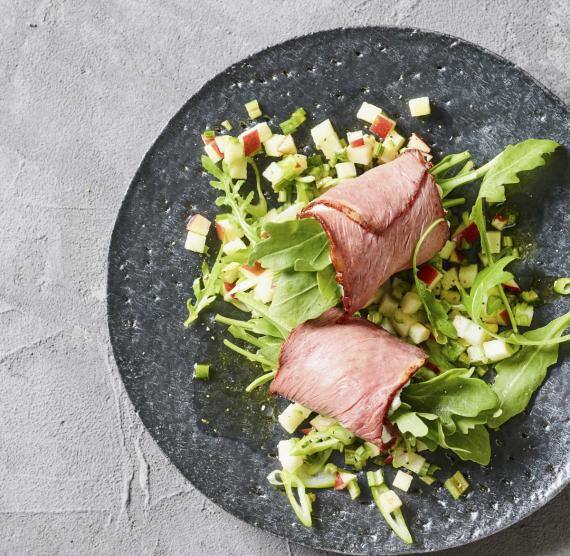 Roastbeef Röllchen angerichtet auf Salat auf einem dunklen Teller mit rustikalem Besteck