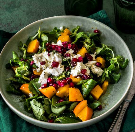 Feldsalat mit Kürbiswürfeln, Feta und Granatapfel auf Teller mit Beteck