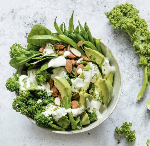 Bowl mit Grünkohl, Brokkoli, grünen Bohnen, Babyspinat, Avocado und Mandeln, darüber Joghurt-Dressing