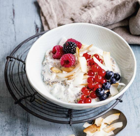Schüssel mit Kokos-Hanf-Chia-Creme, darüber Beeren und Kokoschips