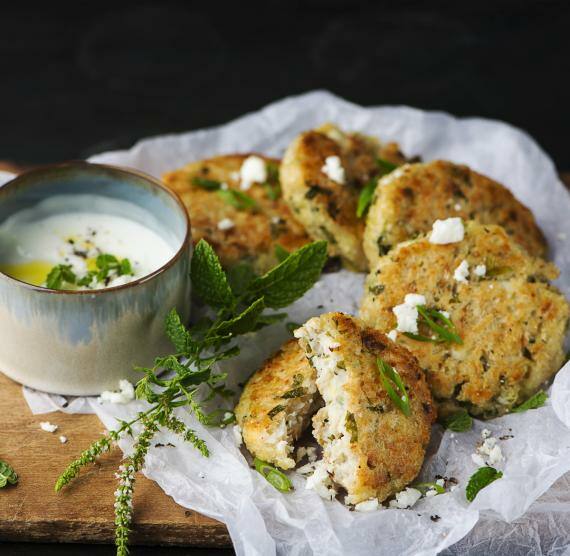Blumenkohl-Frikadellen auf Butterbrotpapier, mit Minze und Feta bestreut, daneben ein Joghurt-Dip