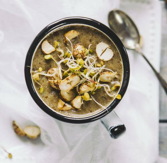 Tasse mit brauner Suppe, darin Haselnüsse und Sprossen