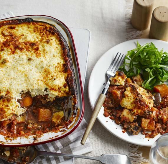 Auflaufform mit Moussaka, daneben Teller mit einer Portion davon plus Salat