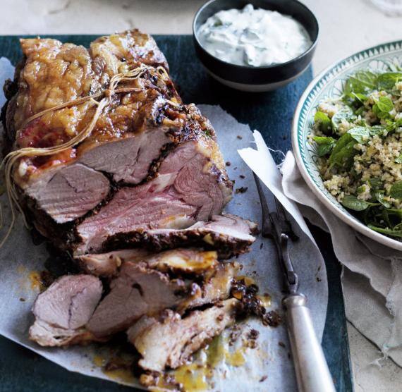 Angeschnittener Lammbraten auf schwarzem Brett, daneben Teller mit Salat