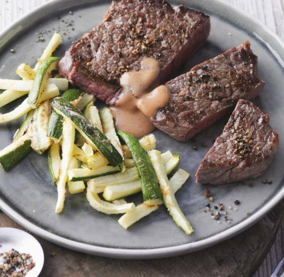 Steakstücke neben Zucchinistreifen und Sauce auf einem Teller