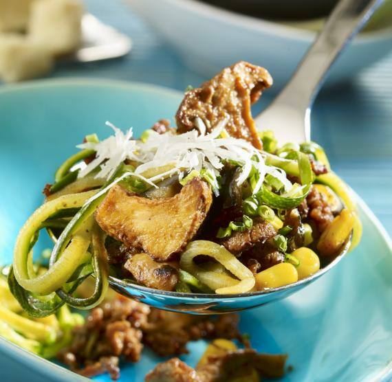 Schöpflöffel mit Gemüse und Fleisch über einem Teller