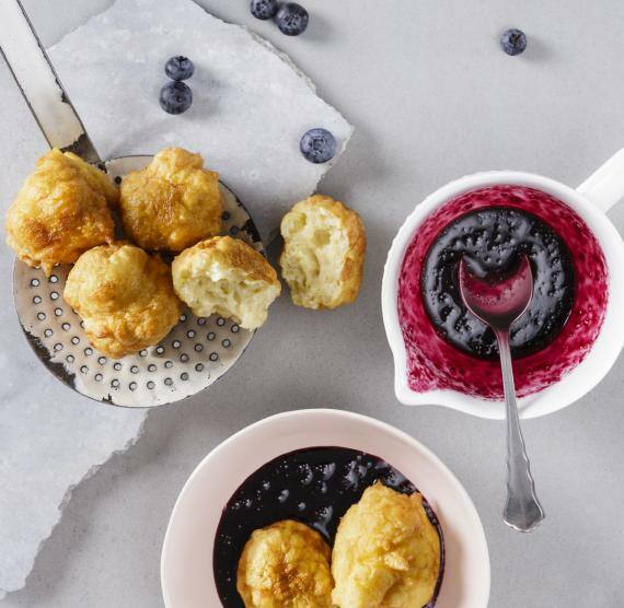 Quarkbällchen auf einem Schaumlöffel, daneben Blaubeersauce