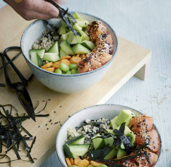 Jemand garniert eine Schale gefüllt mit Lachs, Edamame und Blumenkohlreis