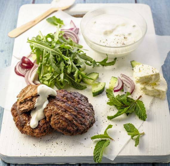 Burgerpatty auf einem Holzbrett mit Salat und Joghurtsauce