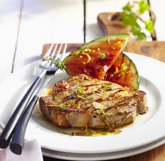 Mariniertes Schweinsfleisch neben einem Stück Wassermelone auf einem Teller im Garten