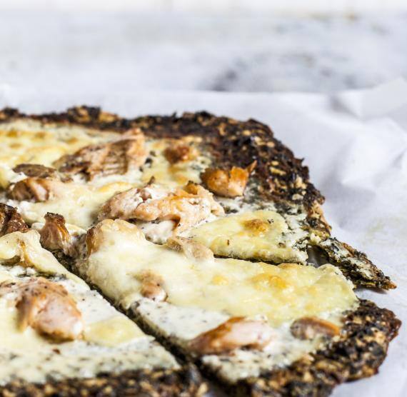 Dünne Pizza auf einem mit Backpapier belegten Holzbrett