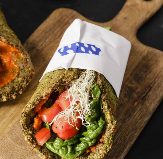 Wrap aus Grünkohl mit würziger Salatfüllung eingewickelt in Esspapier auf einem Holzbrett