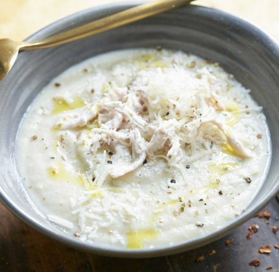 Suppe in einer grauen Schale mit goldenem Löffel auf einem Holztisch