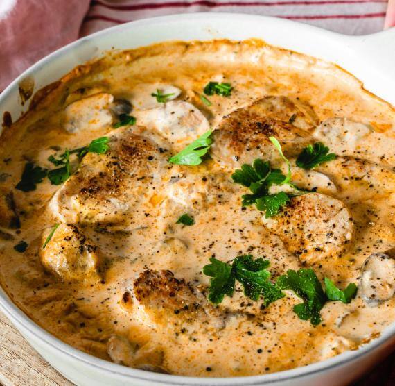 Auflaufform mit Rahmsoße und Schweinefilets wird auf einen Tisch gestellet